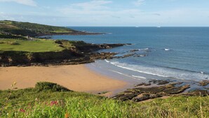 A coastal landscape with a sandy beach, rocky shoreline, and grassy hills. - Caravan 7 (Plymouth)