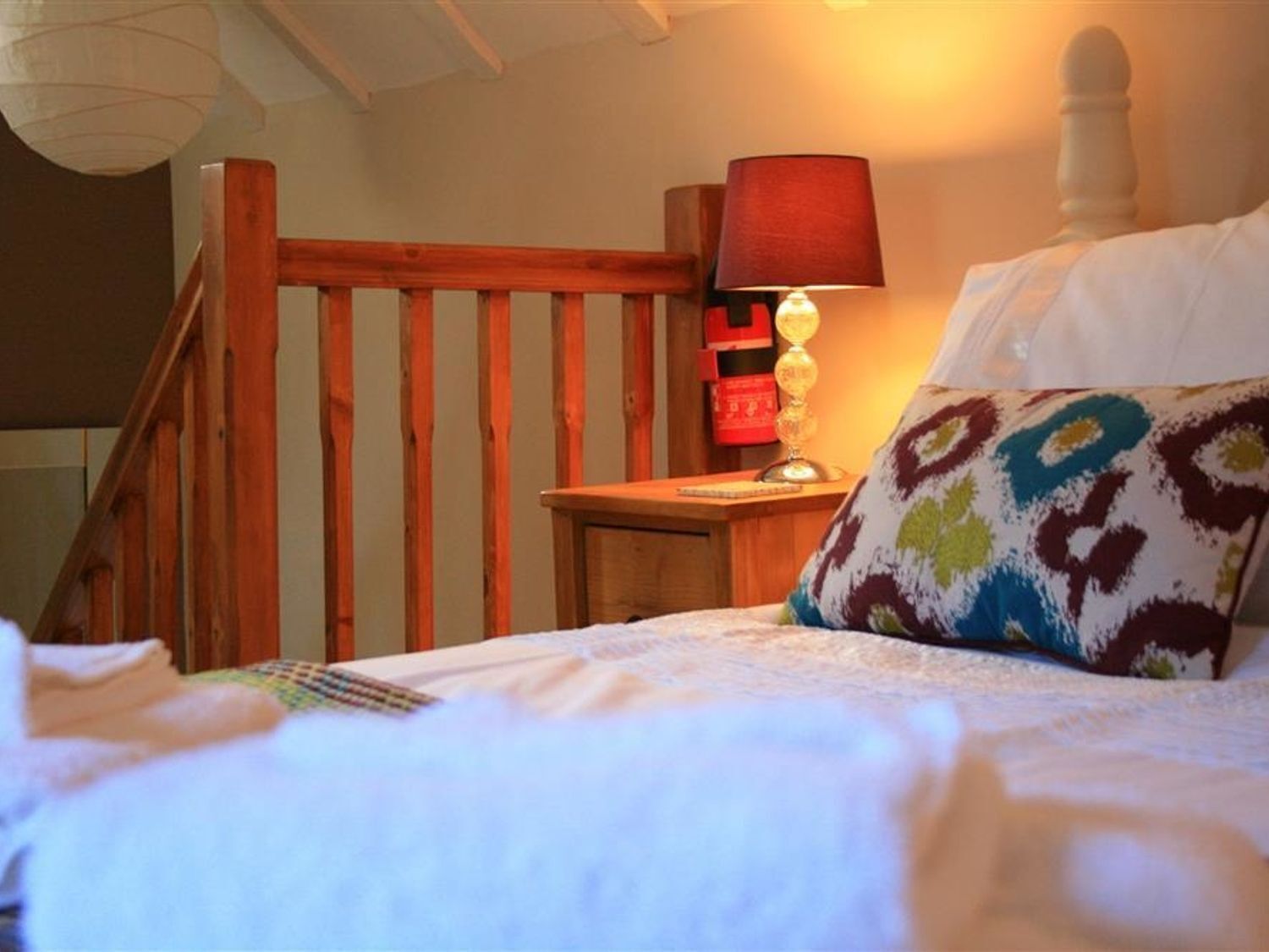 Une chambre avec un escalier en bois, une table de chevet avec une lampe et un coussin à motifs.