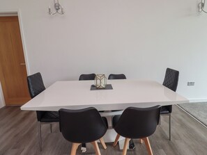 A modern dining area with a white table, black chairs, and a geometric decorative piece. - Otters Cove (Belford)