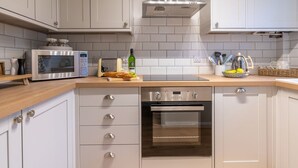 Una cocina moderna con gabinetes blancos, un extractor de acero inoxidable, horno empotrado, microondas y tostadora.