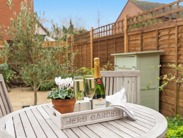 A wooden table with a sign reading "HERB GARDEN," a bottle of champagne, and two glasses on it.