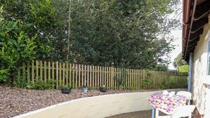 A curved patio with a table and chairs, surrounded by a wooden fence and greenery. - Paws-a-while (Norwich)