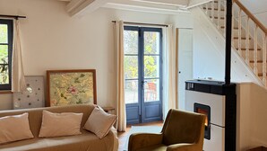 A cozy living room with a wooden floor, a sofa, a chair, a coffee table with books, a fireplace, and a staircase. - Charming house, Close to Geneva, Annecy, ski slopes, at the foot of the Salève mountains (etrembiers)