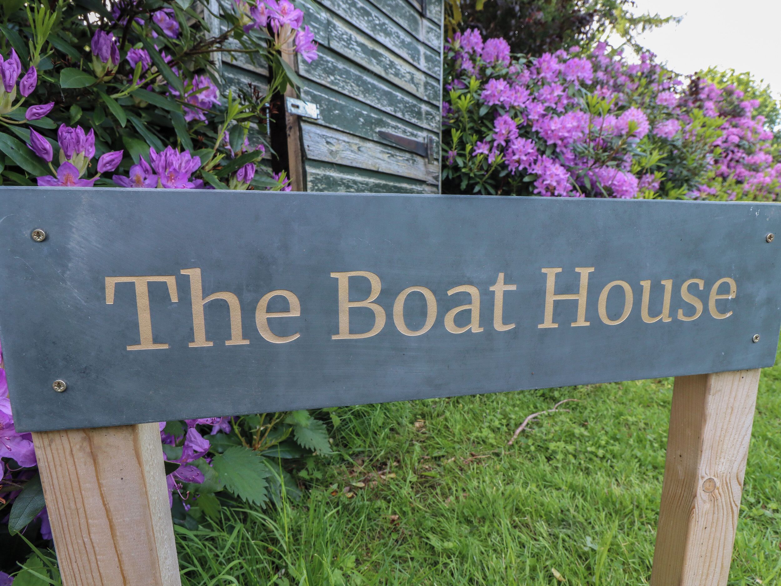 A sign with the text "The Boat House" mounted on a wooden post.