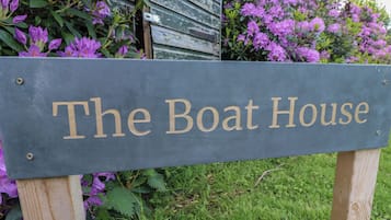 A sign with the text "The Boat House" mounted on a wooden post.