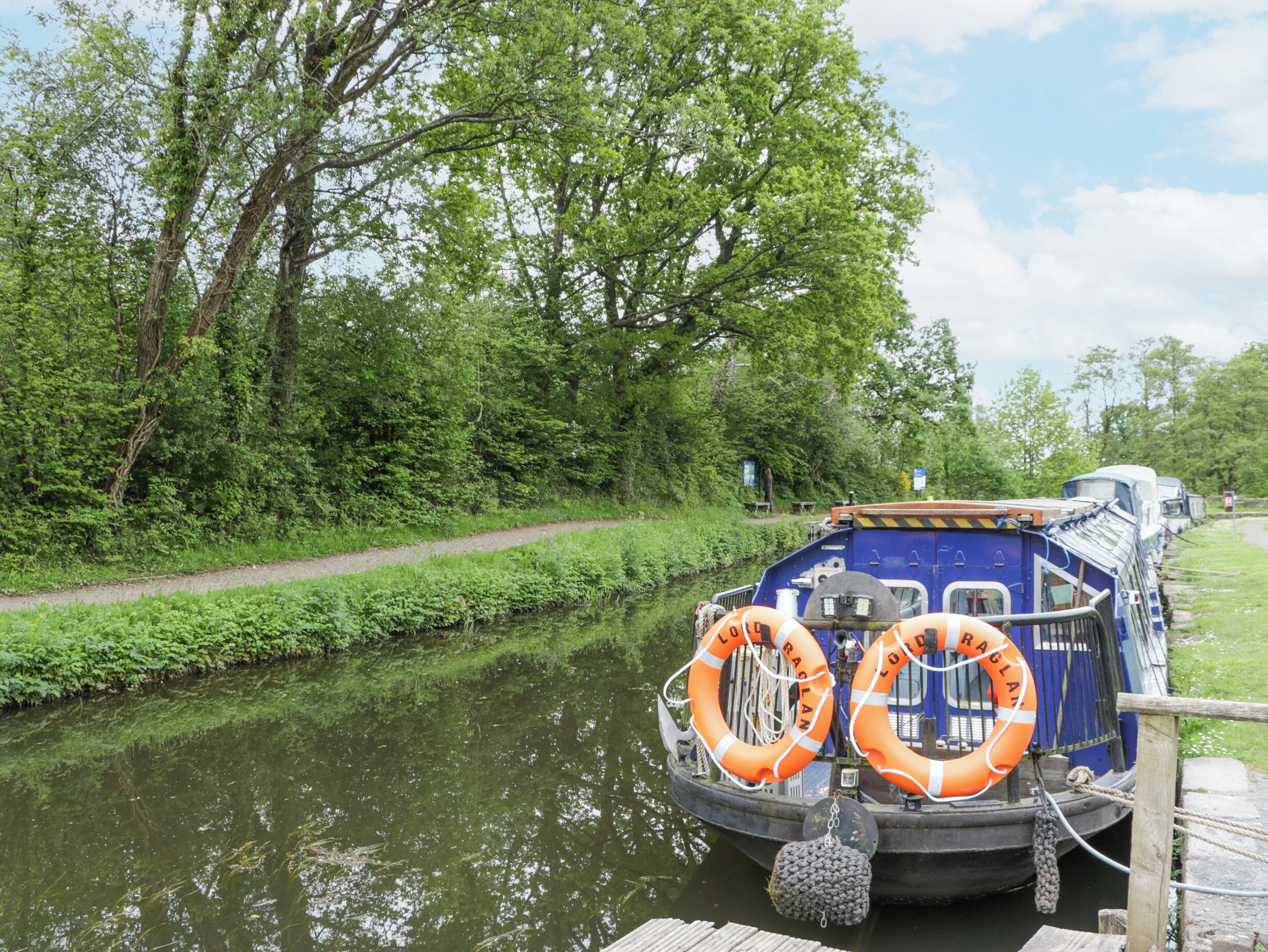 A blue boat docked at a pier with two orange lifebuoys attached to its side.