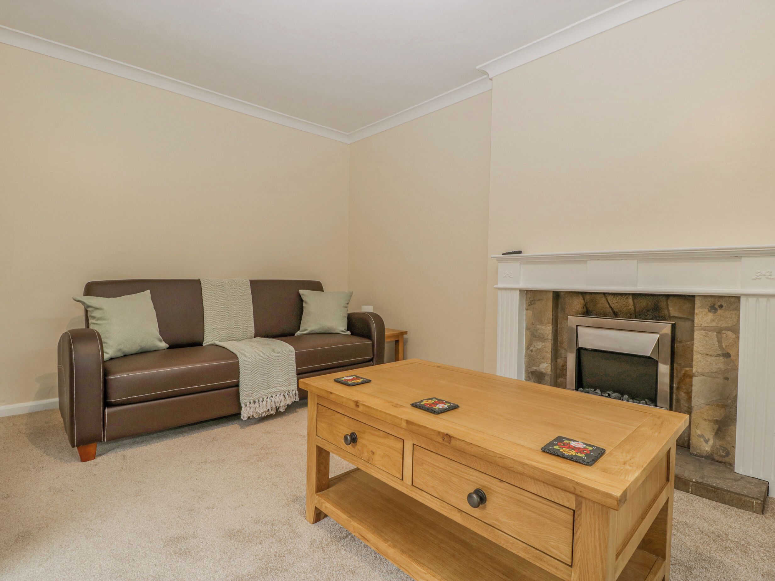 A living room with a brown leather sofa, a wooden coffee table, and a fireplace.