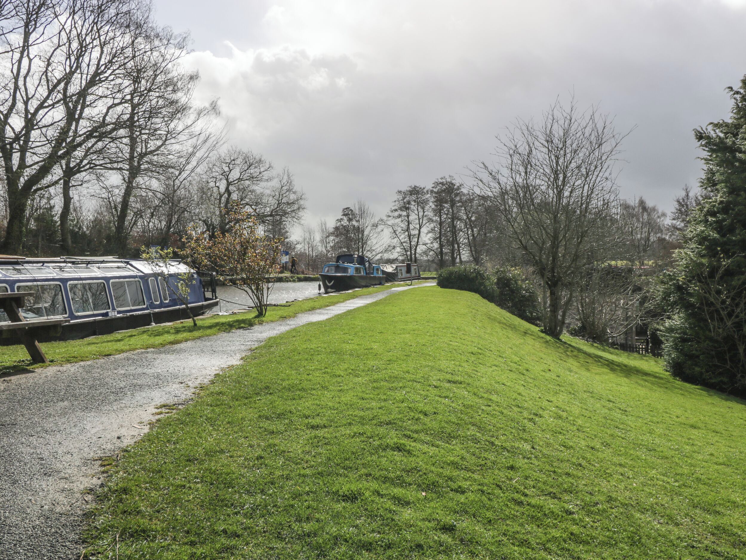 Une zone herbeuse avec un sentier, un train bleu et un bateau amarré au bord de l’eau.