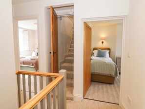 A hotel room with a bed, a nightstand, a lamp, a window, and a staircase. - Bay House Cottage (Broadway)