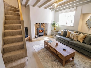 A living room with a fireplace, sofa, coffee table, and a staircase. - Bay House Cottage (Broadway)