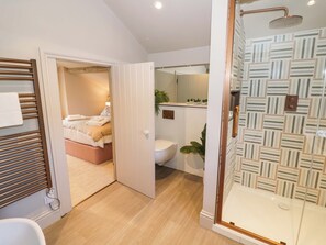 A modern bathroom with a shower, toilet, and a bed in the adjacent room. - Bay House Cottage (Broadway)