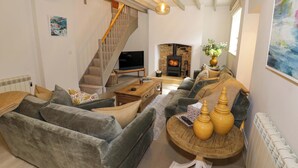 A living room with a sofa, a coffee table, a fireplace, a TV, and a staircase. - Bay House Cottage (Broadway)