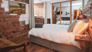 A bedroom with a brick wall, a bed with white bedding, a wooden chair, and a view of a stone wall through a window. - Monastery Hall (Chester)