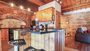 A rustic kitchen with wooden cabinets, a stone wall, and a bar area with stools. - Monastery Hall (Chester)