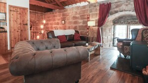 A cozy living room with a stone wall, wooden ceiling beams, a leather sofa, and a fireplace. - Monastery Hall (Chester)