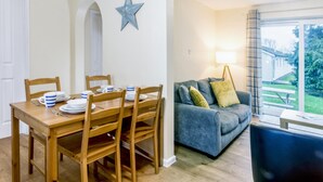 A dining area with a wooden table and chairs, a blue star decoration on the wall, and a grey sofa with cushions. - Chalet 2 at Landscove Holiday Park (Brixham)