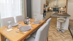 Eine moderne Küche mit weißen Schränken, einem Holzespeisetisch für vier Personen und einer Bar mit Hockern.