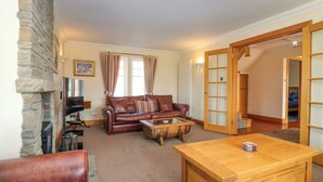 A cozy living room with a stone fireplace, leather sofa, wooden coffee table, and a TV. - Drummygar Mains (Arbroath)