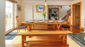 A dining area with a wooden table set for six, a bench, and a vase of flowers. - Drummygar Mains (Arbroath)