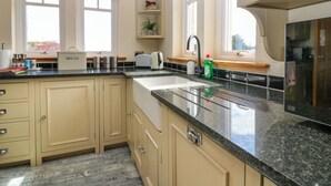 A kitchen with beige cabinets, a granite countertop, a toaster, a sink, and a window with a view of trees. - Drummygar Mains (Arbroath)