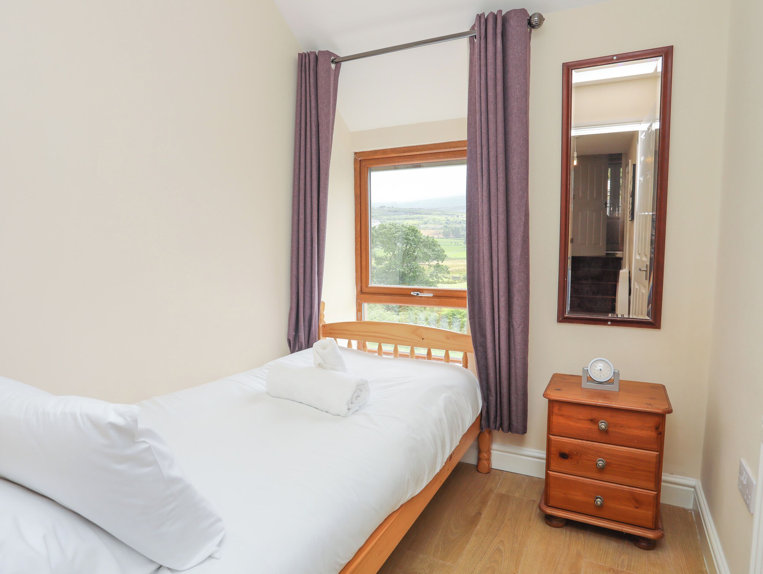 A bedroom with a wooden bed, a dresser, a window with curtains, and a mirror.