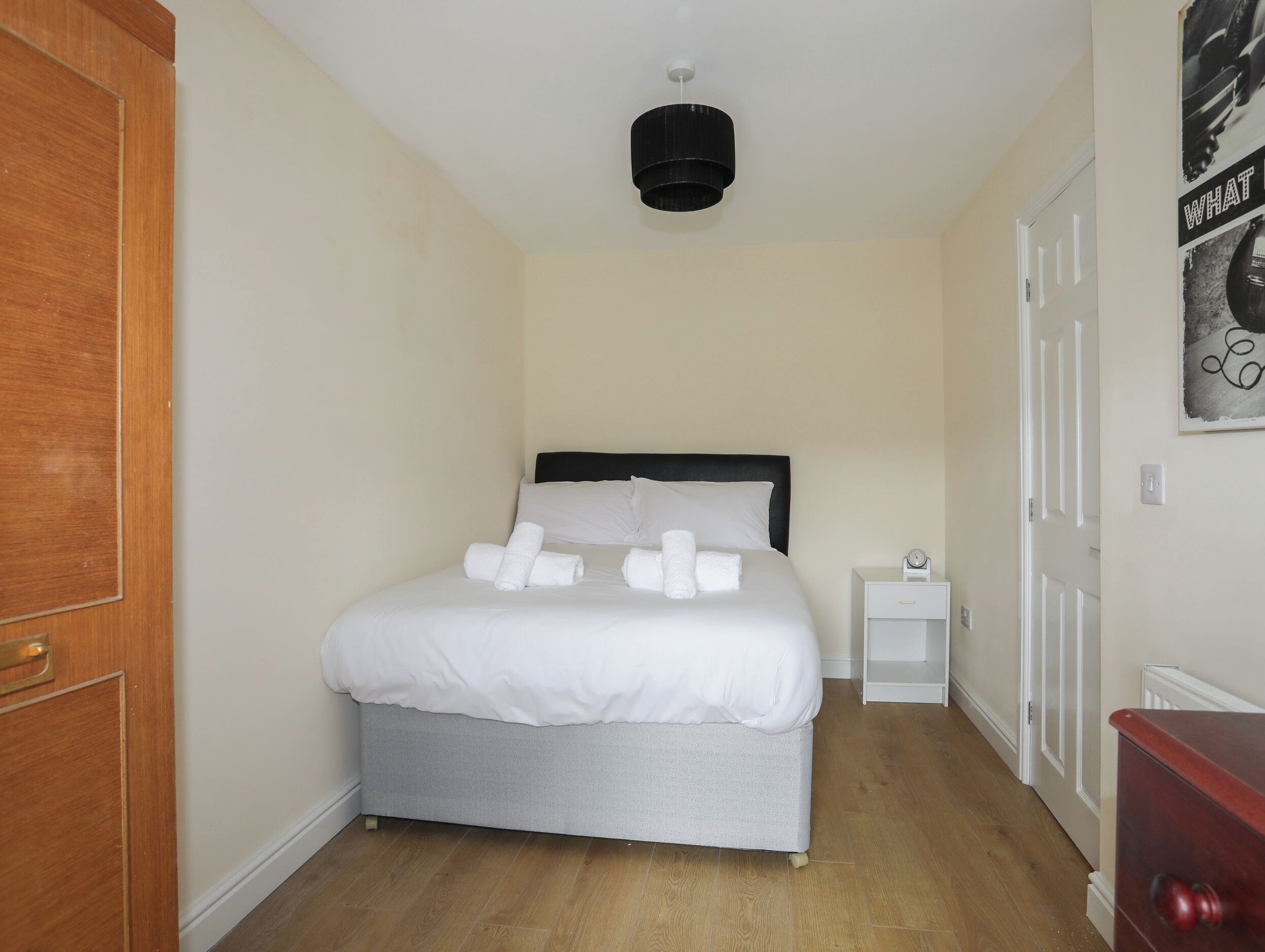 A small, neatly arranged bedroom with a bed, a bedside table, a nightstand, and a door.