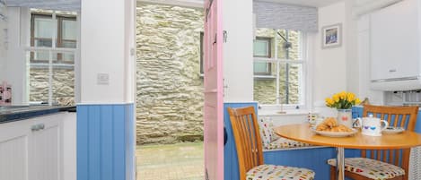 Una cocina con una mesa de madera, sillas y una ventana que da a un muro de piedra.