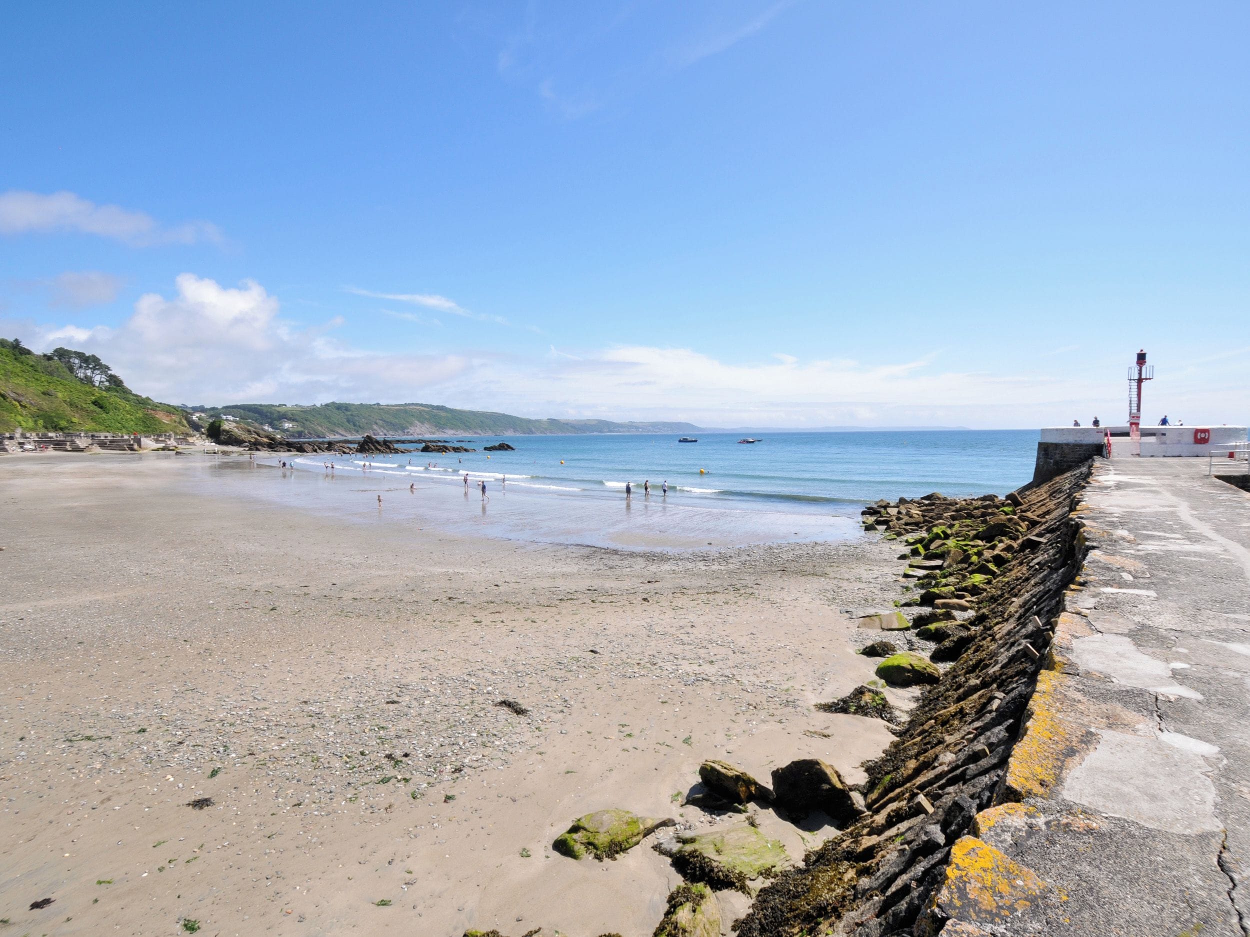 A coastal beach with a rocky breakwater and a lighthouse in the distance.