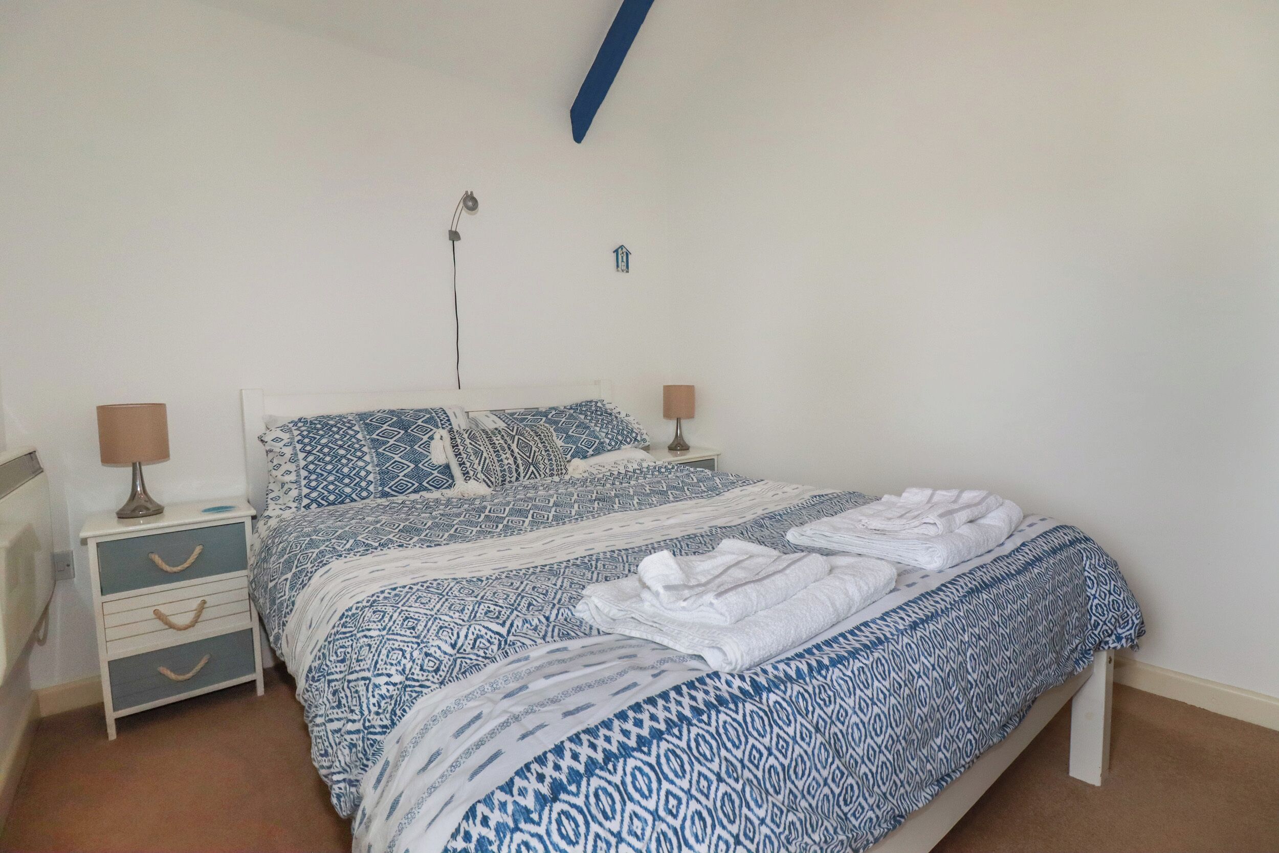 A bedroom with a bed, two bedside tables, and a wall-mounted lamp.