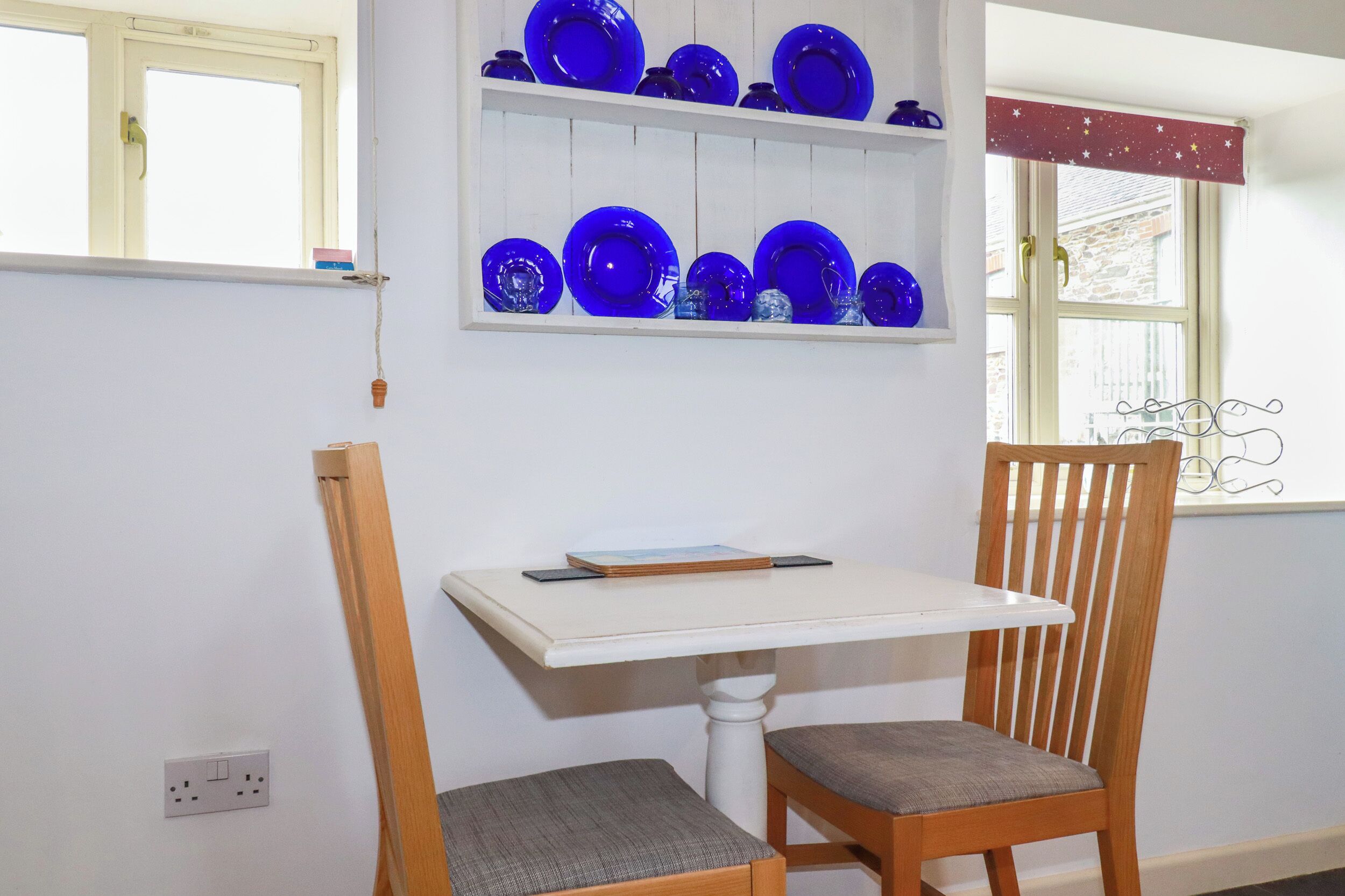 A room with a white table, a wooden chair, and a shelf with blue glassware.