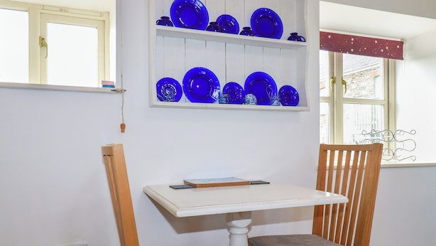 A room with a white table, a wooden chair, and a shelf with blue glassware. - Moonlight (Truro)