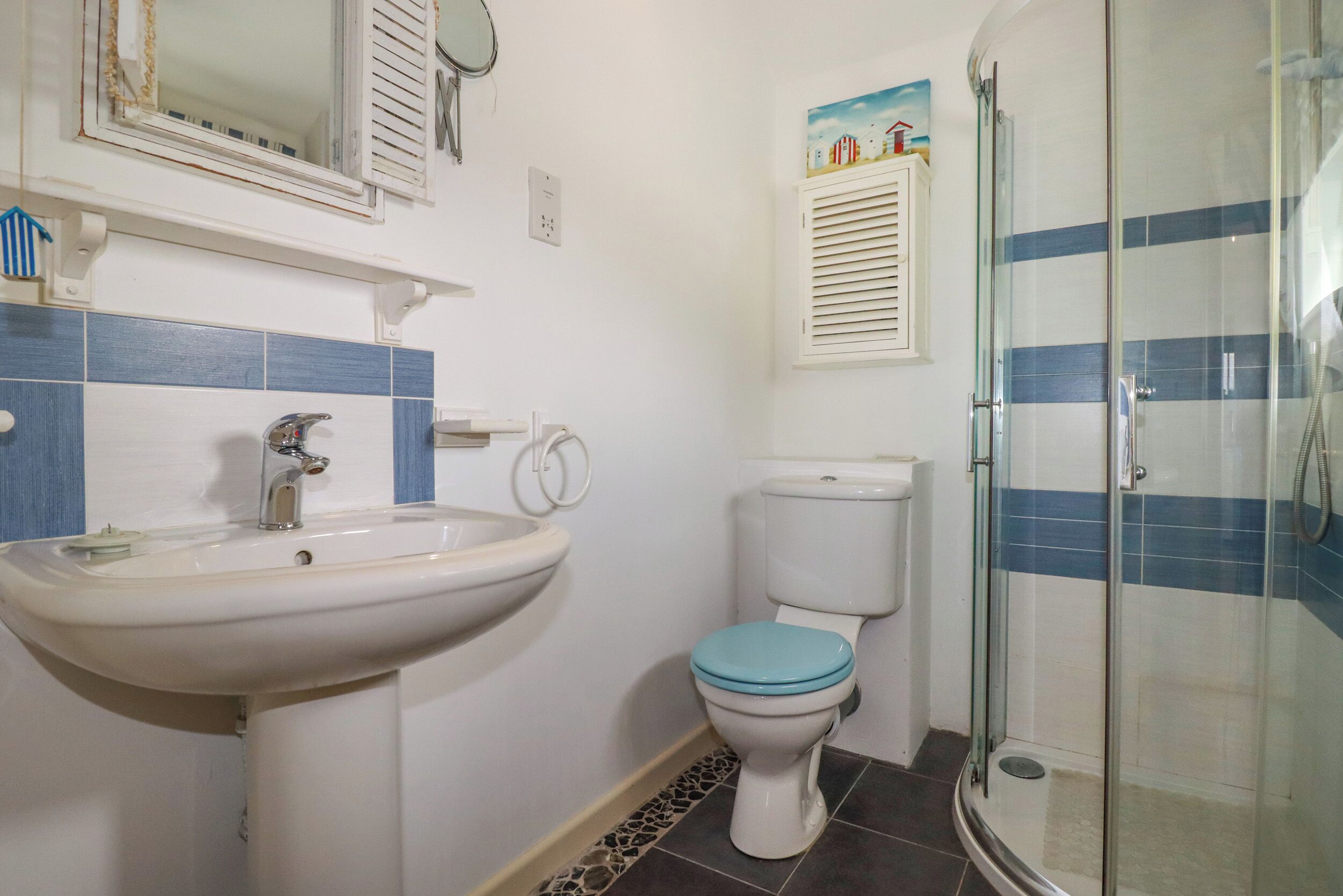 A bathroom with a white sink, blue-striped tiles, a toilet, and a glass-enclosed shower.