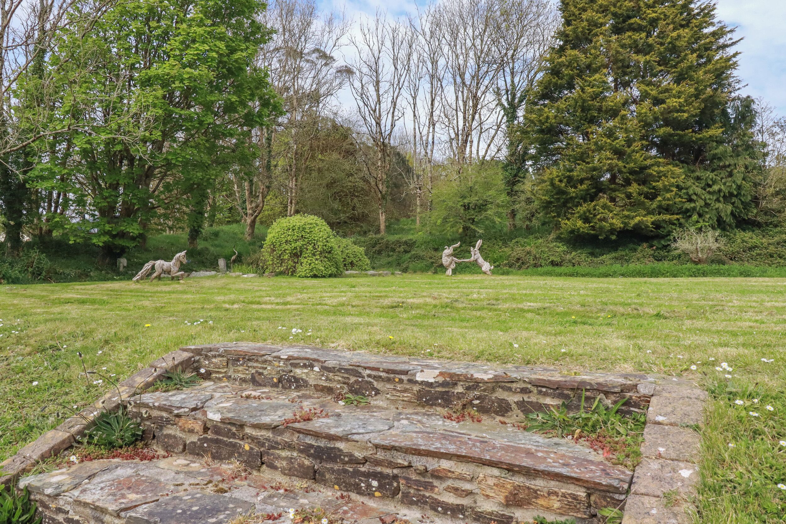 A stone structure in a grassy area with trees and shrubs in the background.