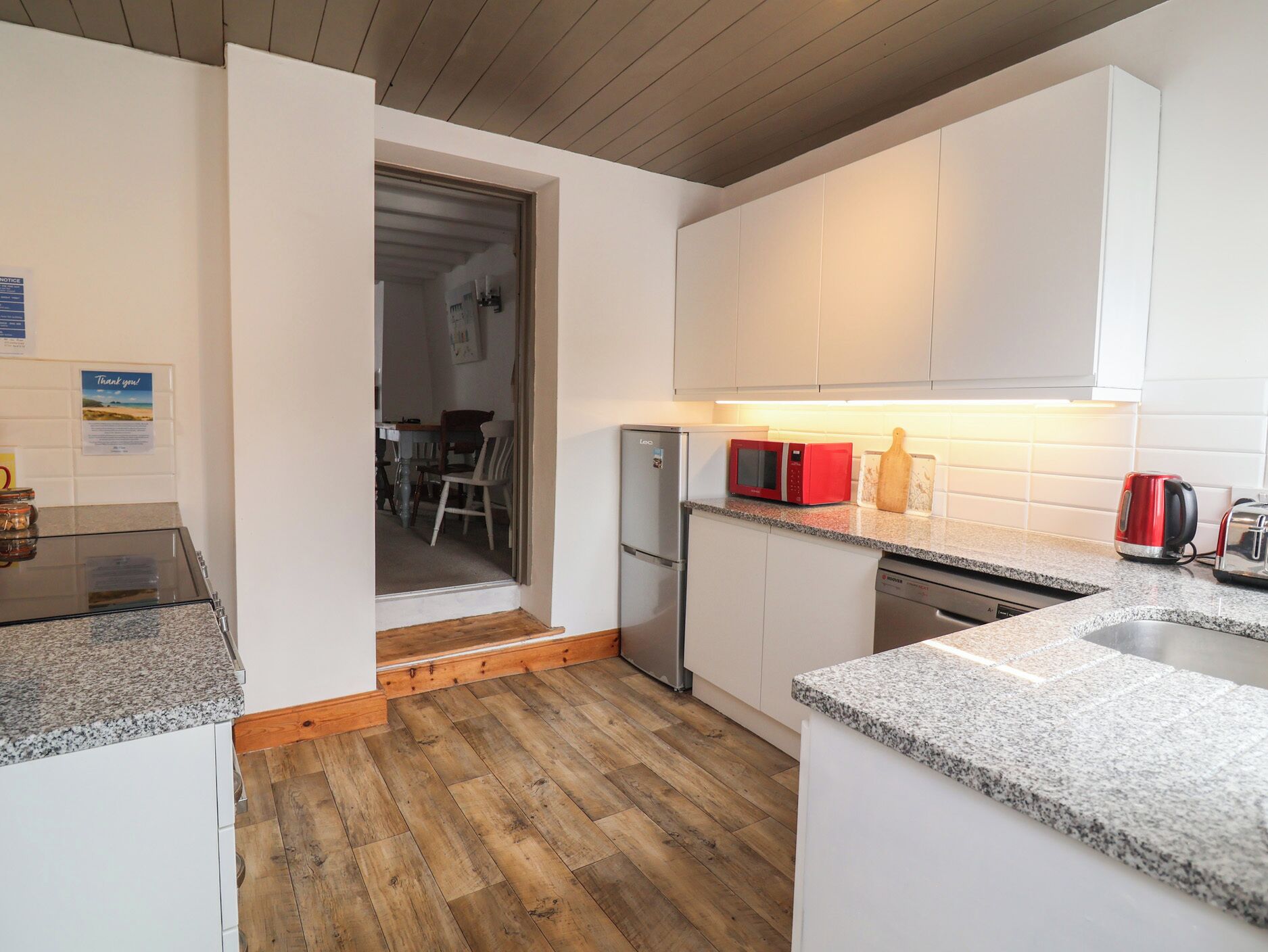 Cocina compacta con gabinetes blancos, microondas, tostadora y lavavajillas.