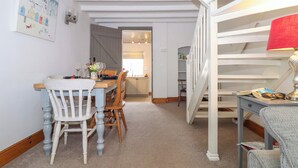 Un coin repas avec une table dressée pour quatre personnes, un escalier et une cuisine visible au fond.
