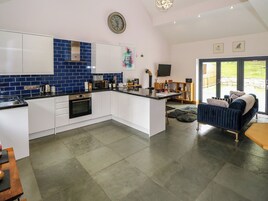 Una cocina moderna con armarios blancos, salpicadero azul y una isla central. Hay una zona de comedor con sofá azul y televisor.