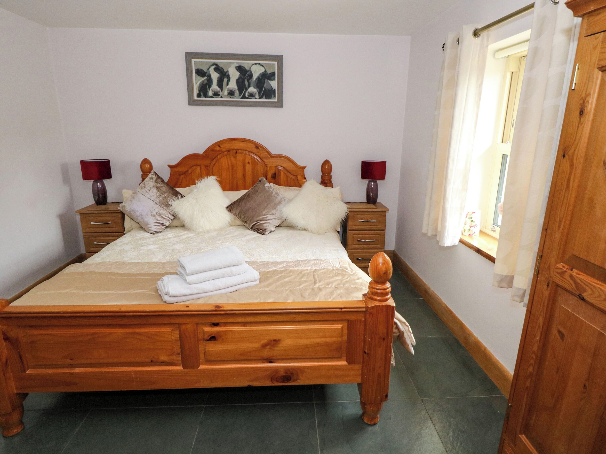 Un lit en bois avec une tête de lit, deux tables de chevet avec des lampes, un oreiller moelleux et une serviette pliée sur le lit.