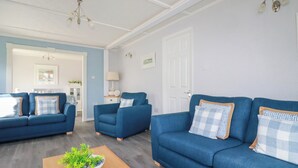 A living room with two blue sofas, a wooden coffee table with a plant, and a white door in the background. - Lowen Lodge (Padstow)