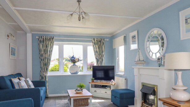 A living room with a blue sofa set, a television, a fireplace, and a window with curtains. - Lowen Lodge (Padstow)