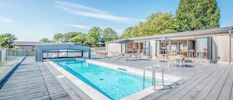 A swimming pool with a wooden deck, lounge chairs, and a covered seating area.