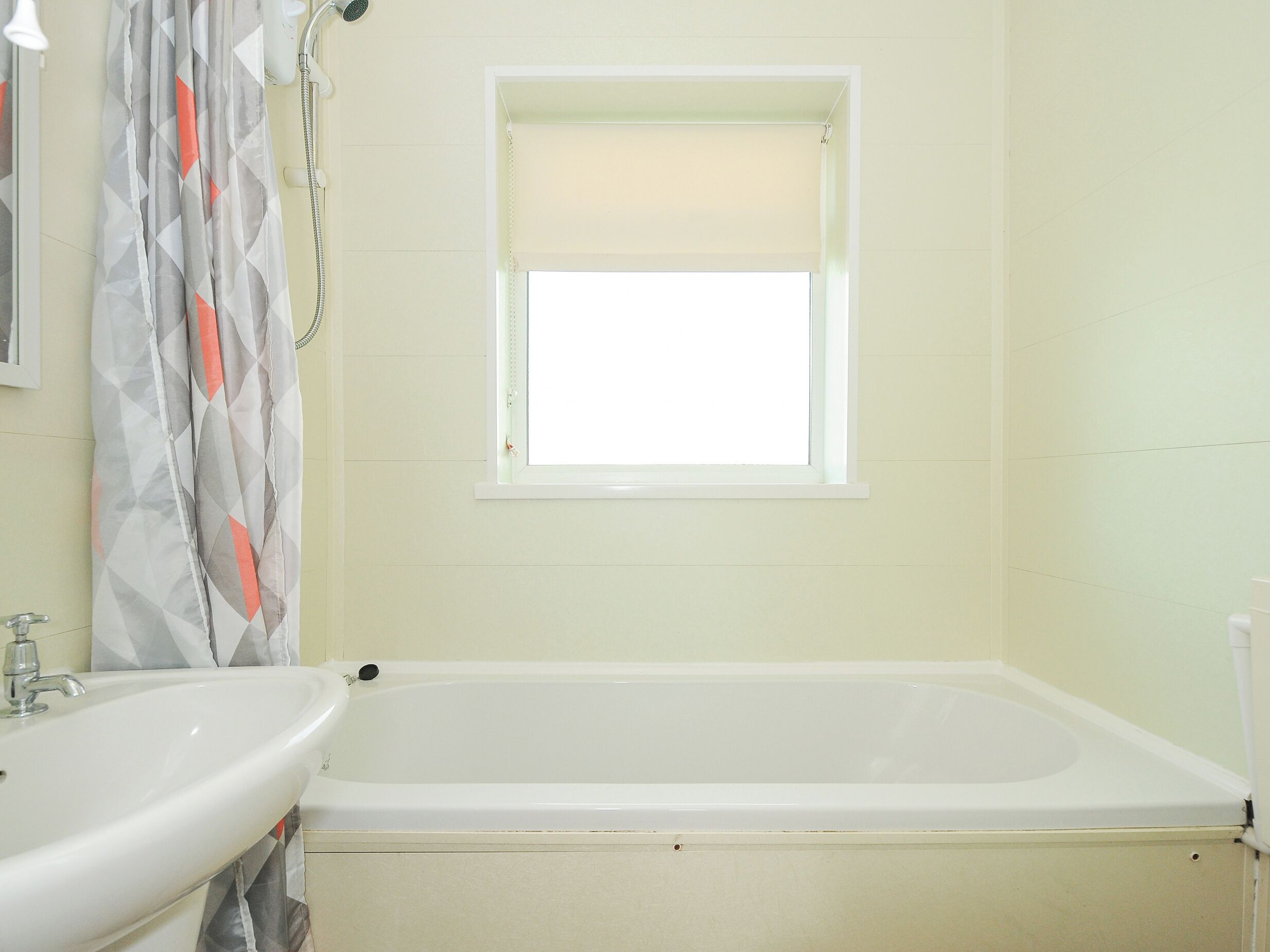 Un baño con bañera, lavamanos y ventana con persiana.