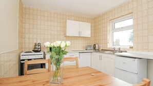 A kitchen with white cabinets, a wooden table, and a vase of white flowers. - Chalet 37 at Landscove Holiday Park (Brixham)