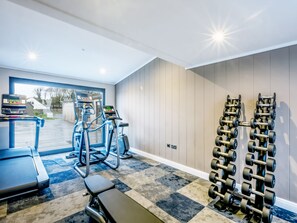 A gym with cardio machines, dumbbells, and a bench.
