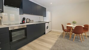 Ett modernt kök med mörka skåp, en inbyggd ugn, en tvättmaskin och en matplats med ett runt bord och stolar.