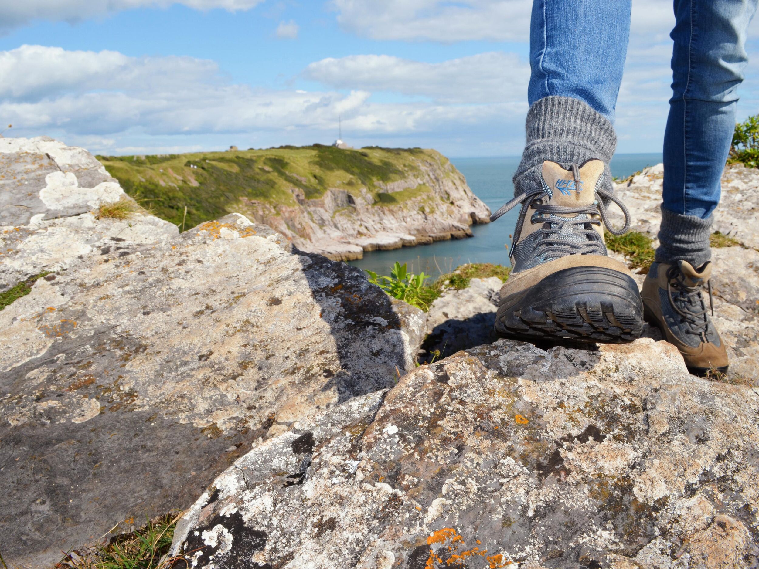 A pair of hiking boots on a rocky surface with a coastal view in the background.