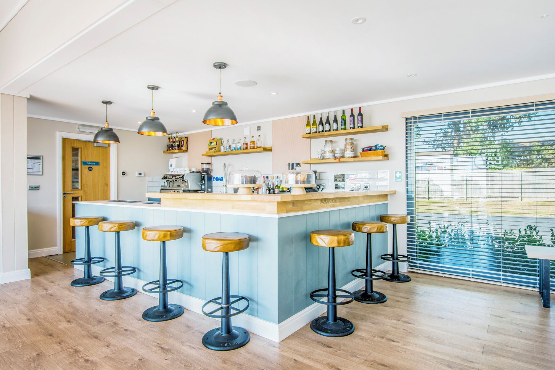 A modern kitchen with a bar area, bar stools, pendant lighting, and a view through the window.