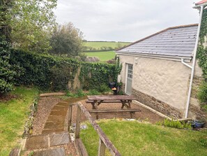Un espace extérieur rustique comprenant un banc en bois, un chemin de pierres et une maison avec un toit en tuiles.