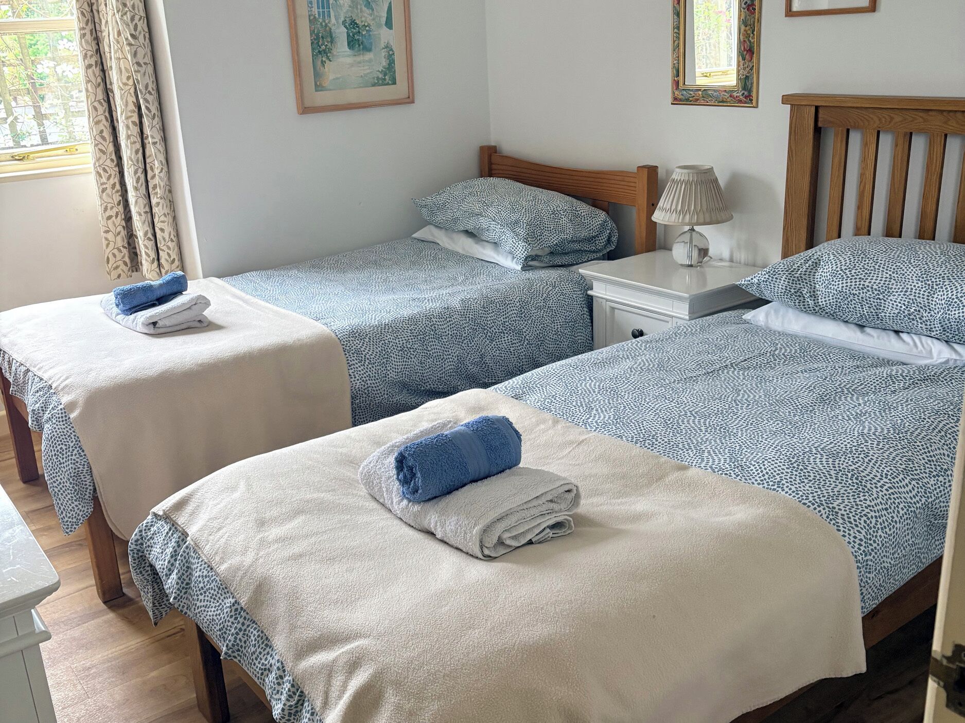 Une chambre d’hôtel avec deux lits, une table de chevet avec une lampe et une fenêtre avec des rideaux.