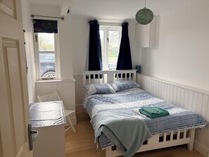 A bedroom with a bed, a window with curtains, a chair, a desk, and a hanging light fixture.