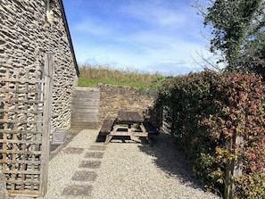A stone building with a wooden fence, a gravel path, and a picnic table.